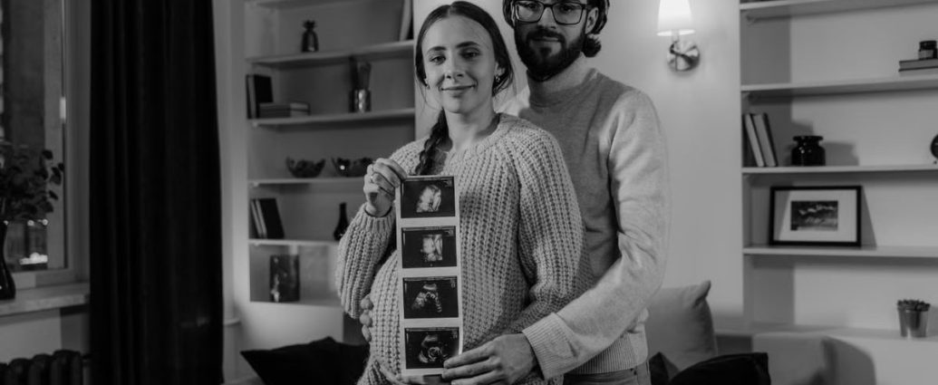 Happy couple at home embracing and displaying ultrasound photos, celebrating pregnancy.