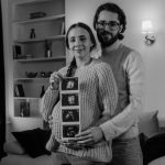 Happy couple at home embracing and displaying ultrasound photos, celebrating pregnancy.