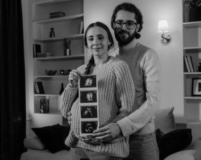Happy couple at home embracing and displaying ultrasound photos, celebrating pregnancy.