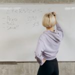 Female writing workout schedule on whiteboard in gym setting.
